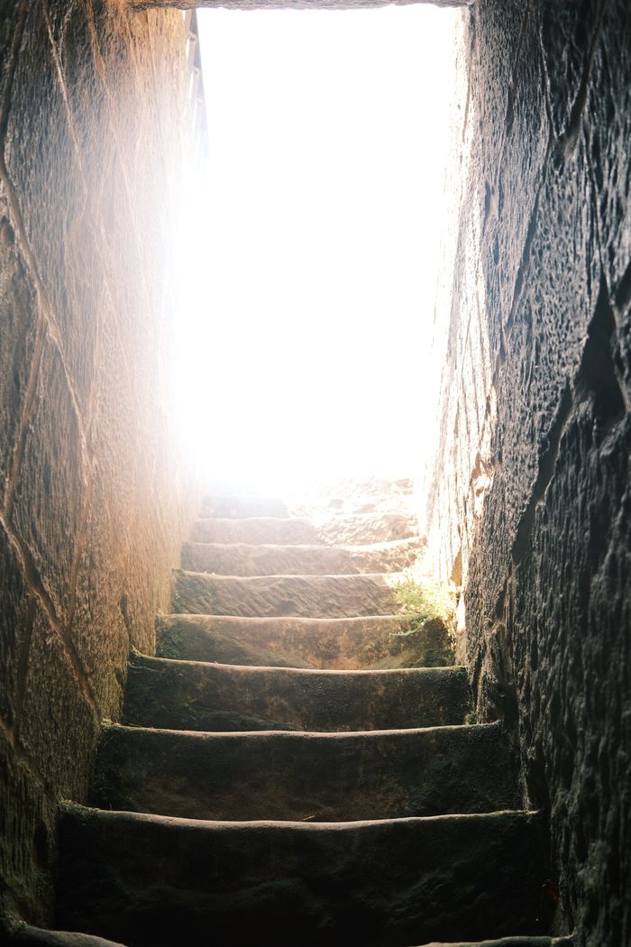 A worn stone stairway leading up to a bright, sunlit exit, creating a dramatic contrast.