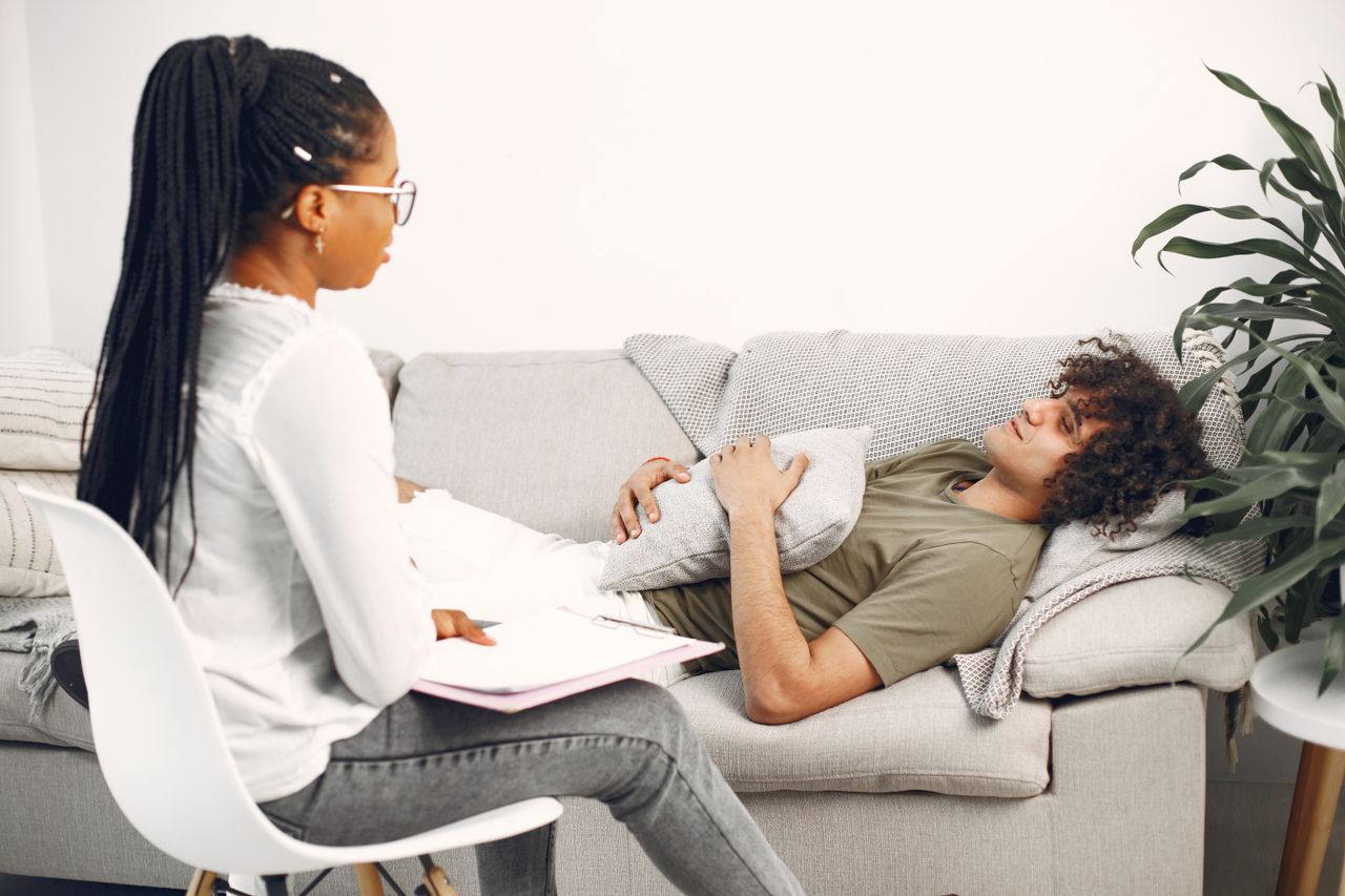 ANUNE Hypnotherapy & Welness Durham NC A man in therapy session, lying on a couch, speaking with a female therapist taking notes.